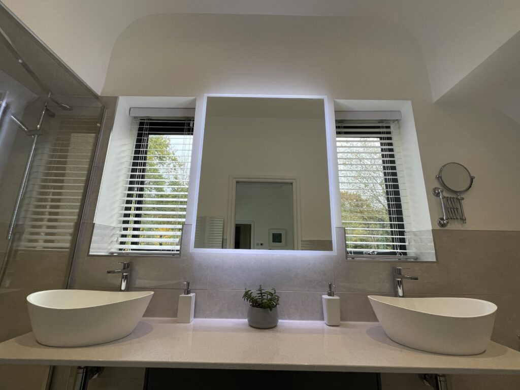 Renovated bathroom with twin basins, a backlit mirror and shuttered windows