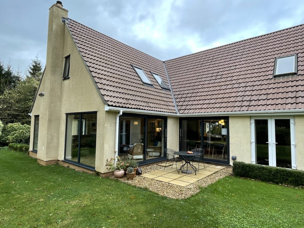 Rendered house with a rear extension, tiled roof and rooflights, seen from the lawn
