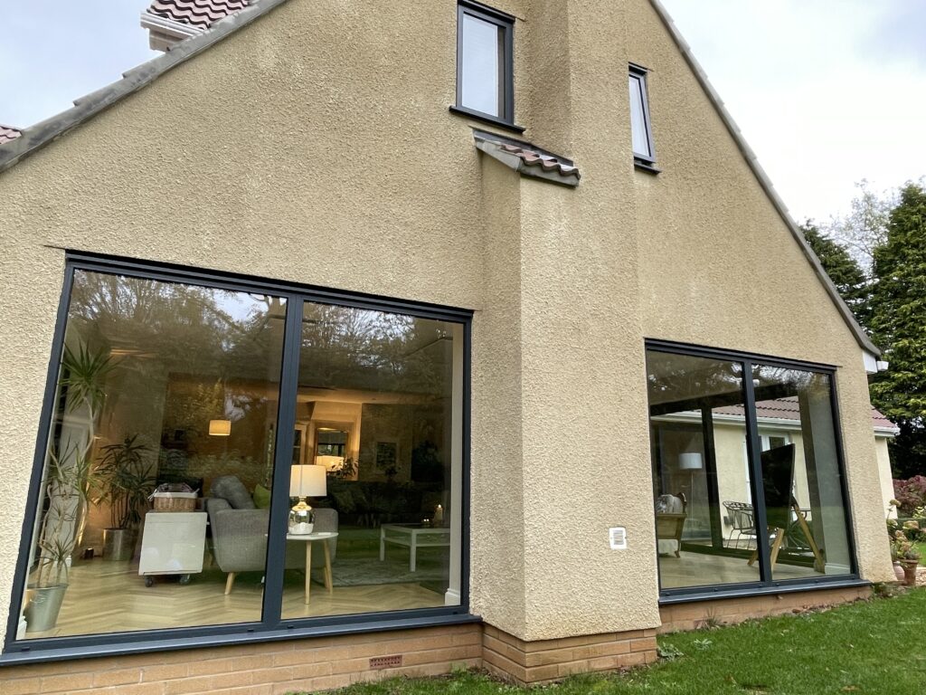 Rear of a rendered house with full-height glazing to a new extension