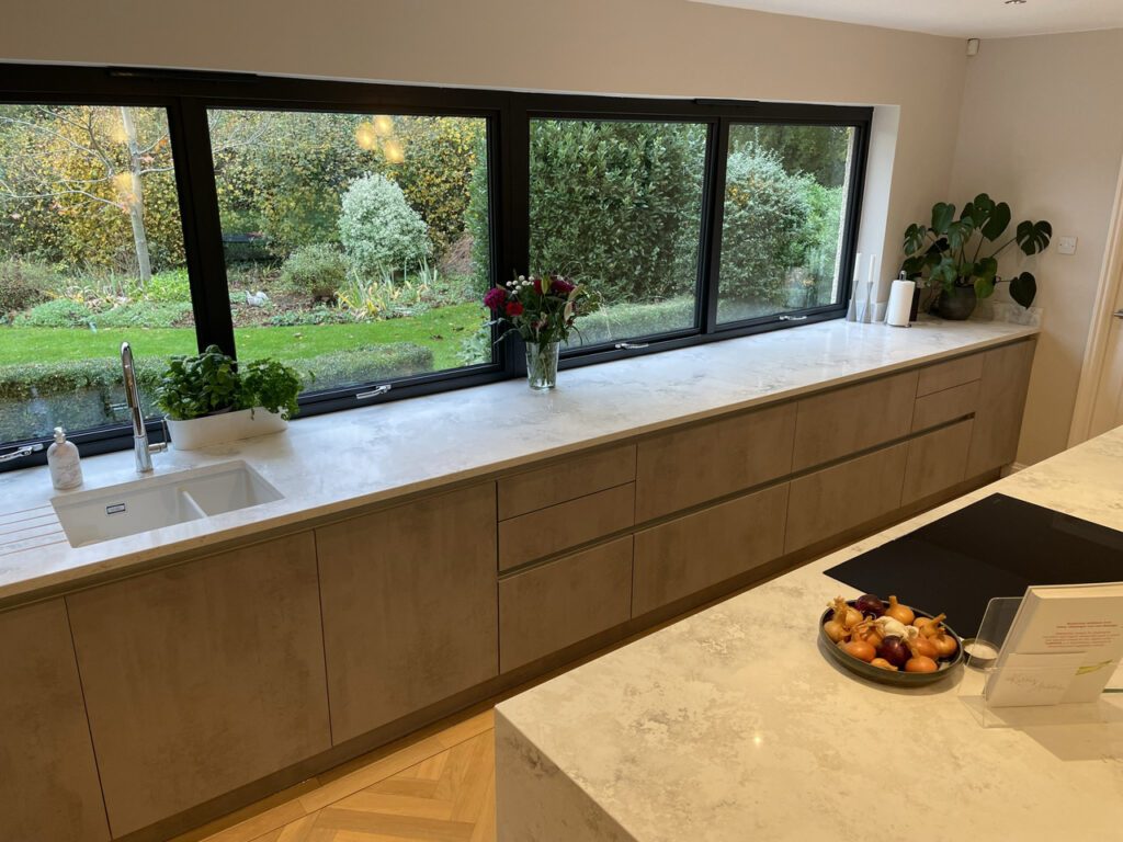 Long kitchen run with a stone worktop and a picture window onto the garden