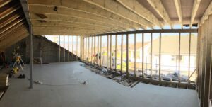Interior mid-build showing a steel and timber frame with full-width glazing onto a sea view