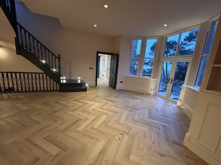 Renovated period reception room with herringbone flooring, a black staircase and bay windows