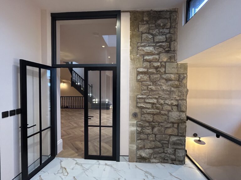 Hallway with Crittall-style glazed doors, an exposed stone wall and marble flooring