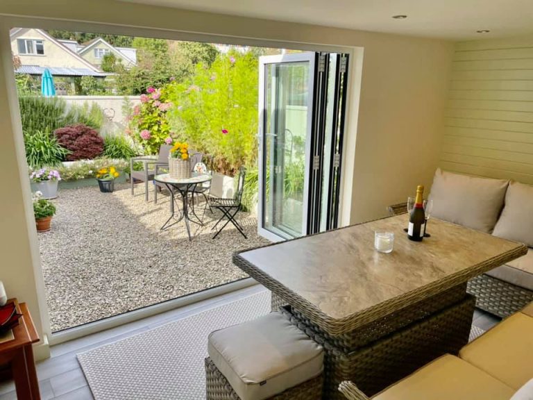Converted garage finished as a garden room, bifold doors open onto a planted patio with table and seating