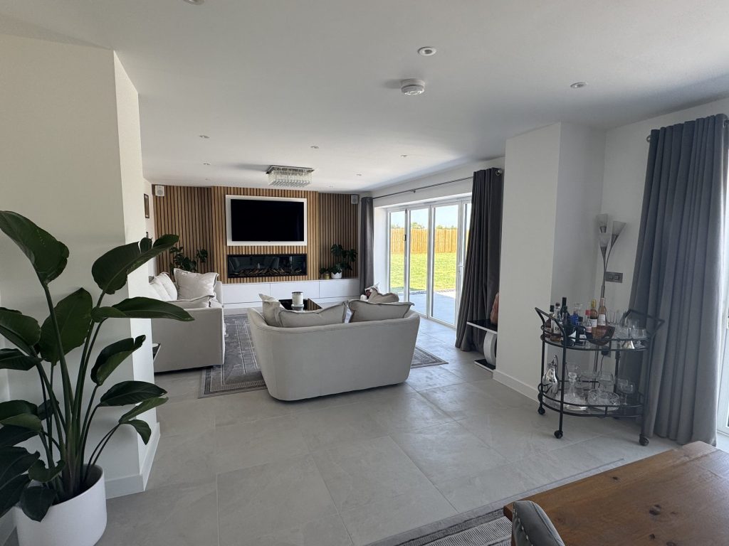 Living room with a wall-mounted television, garden glazing and full-length curtains