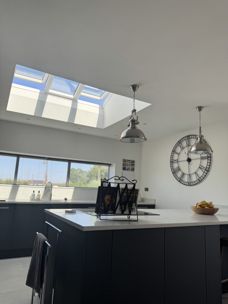 Kitchen with a dark island, rooflights and a large wall clock