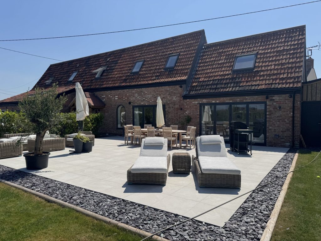 Converted barn with bifold doors onto a paved terrace and sun loungers
