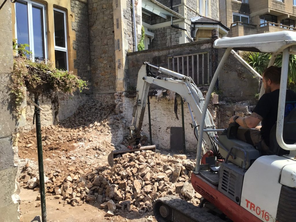 Mini digger clearing rubble where a rear extension is being broken through into a stone period house
