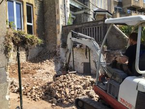 Mini digger clearing rubble where a rear extension is being broken through into a stone period house