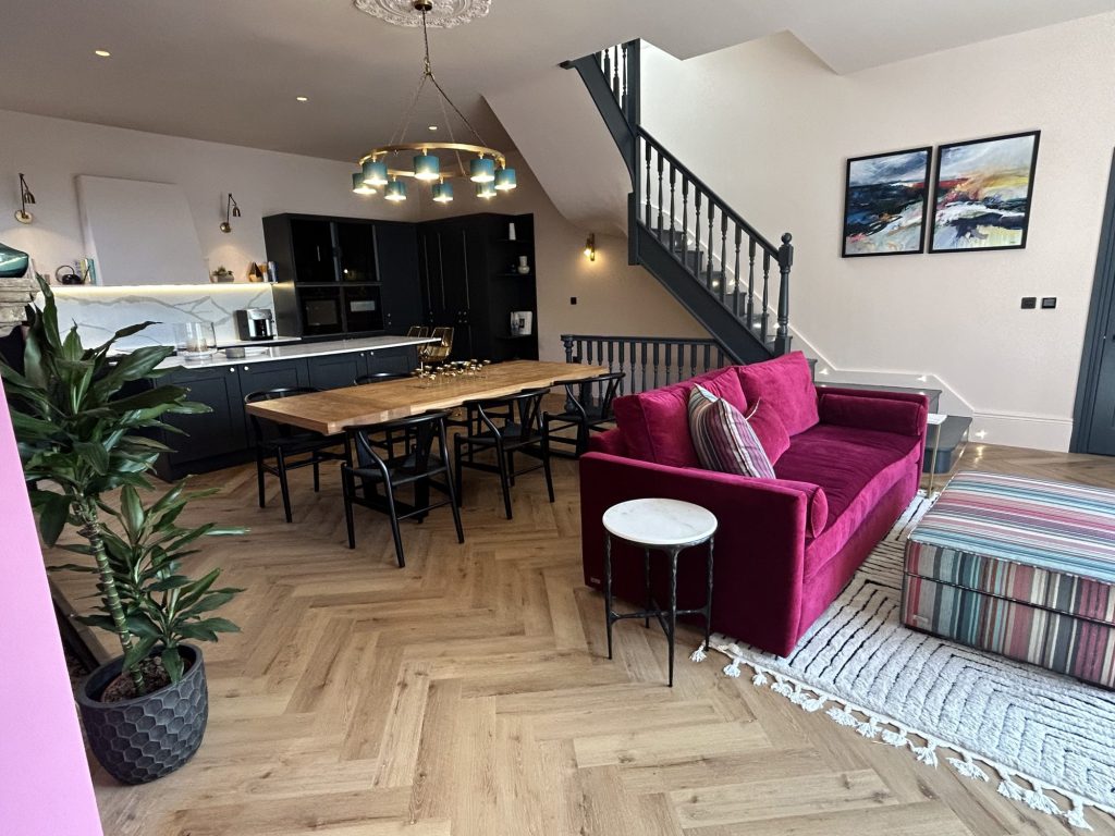 Open-plan living and dining extension with herringbone flooring and a pink velvet sofa