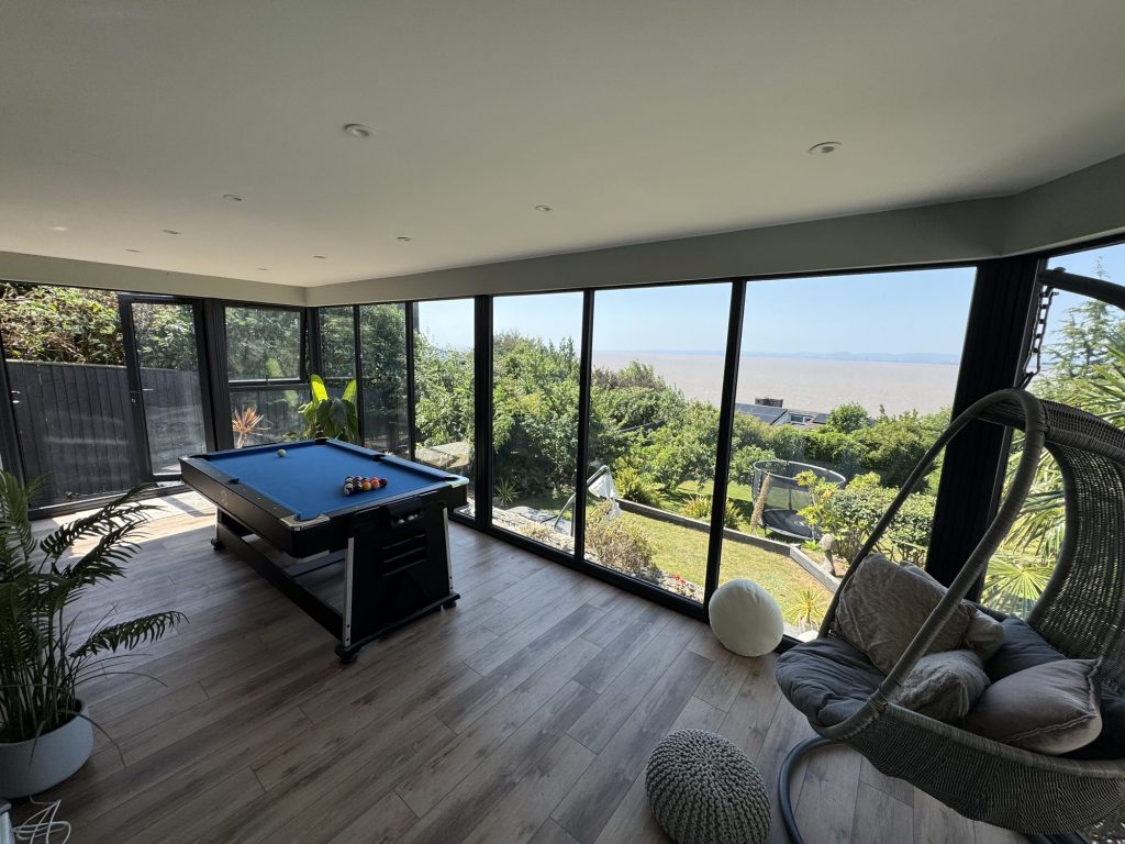 Garden room with a pool table and full-height glazing onto the estuary