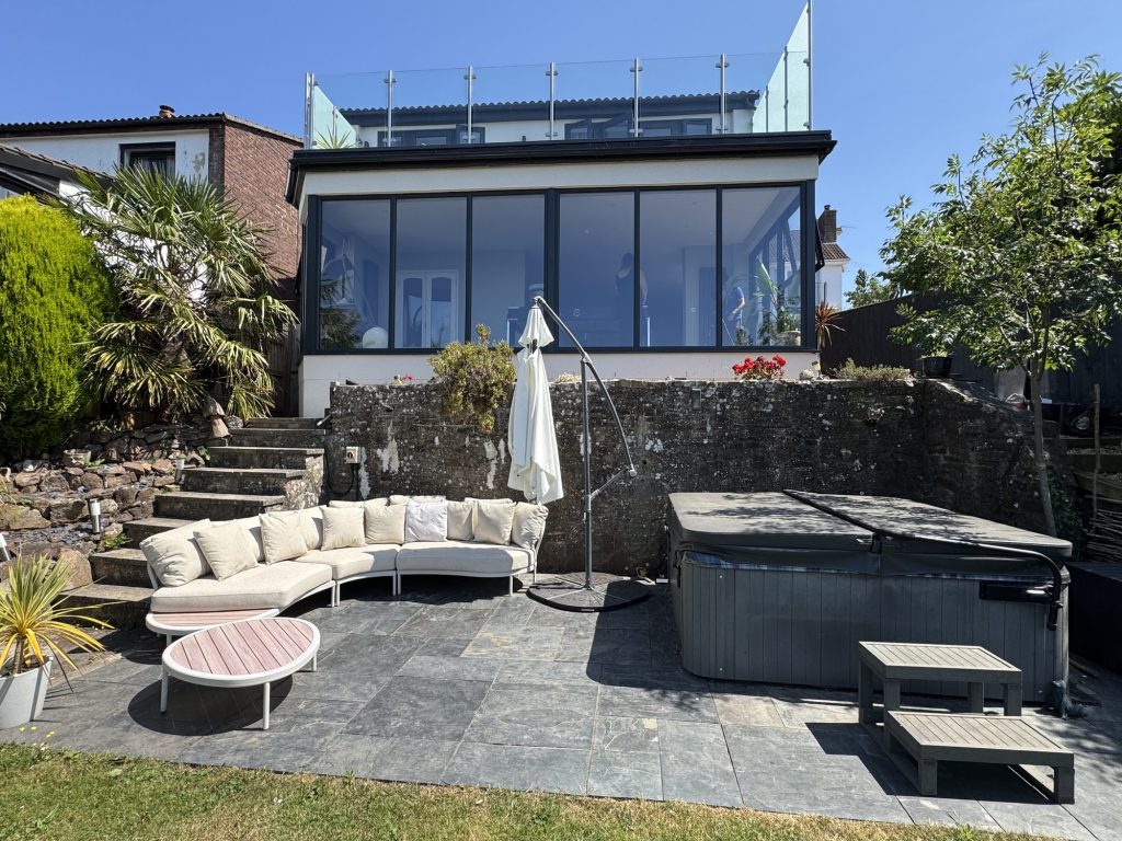 Terraced garden with seating and a hot tub beneath a glazed upper extension