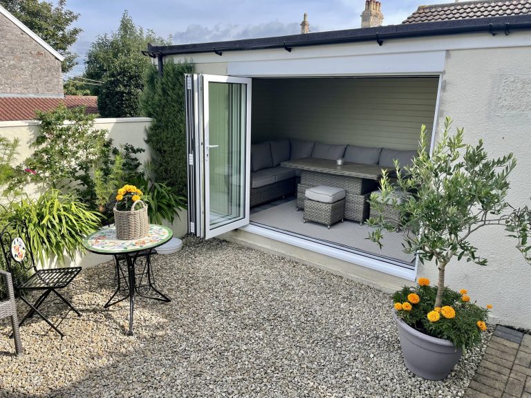 Bifold doors open from a converted garage onto a paved courtyard with seating