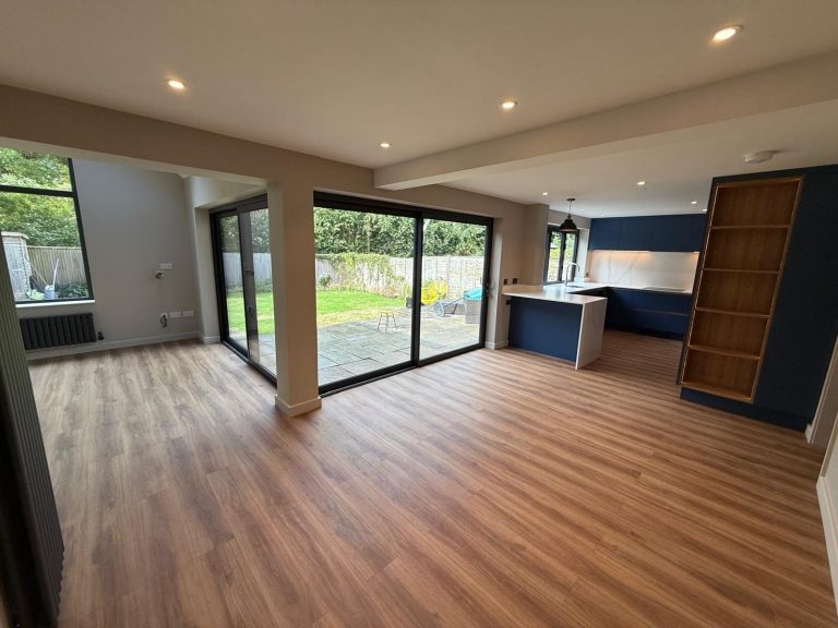 Open-plan kitchen extension with wood flooring, a navy kitchen and sliding doors to the garden