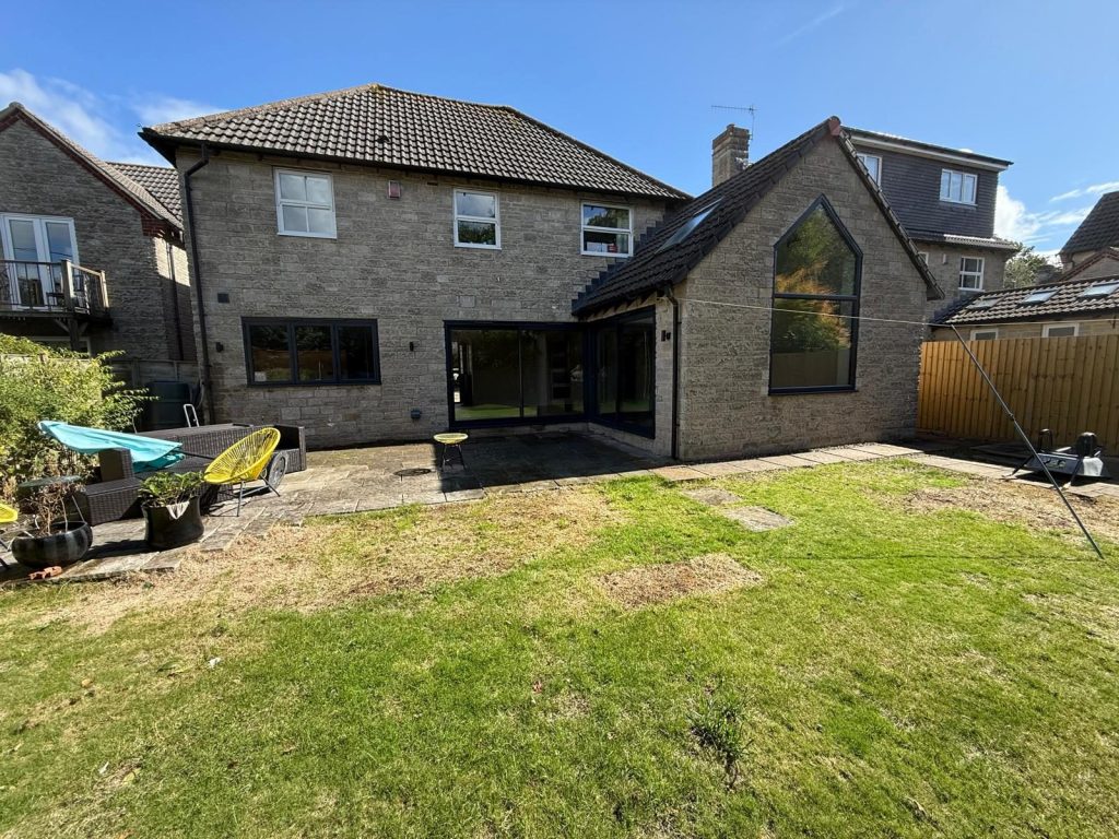Stone house with a rear extension and gabled glazing, seen across the lawn