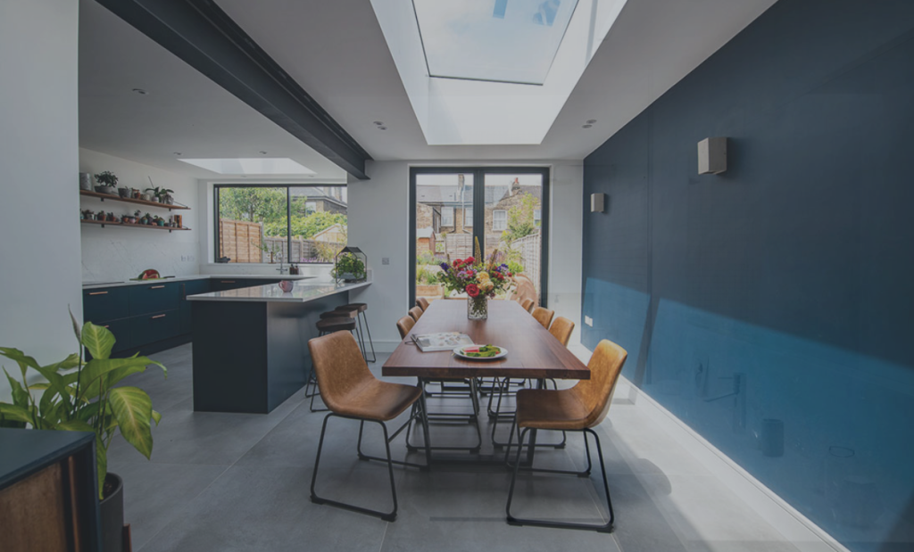 Kitchen and dining area with a blue feature wall, rooflight and tan leather chairs