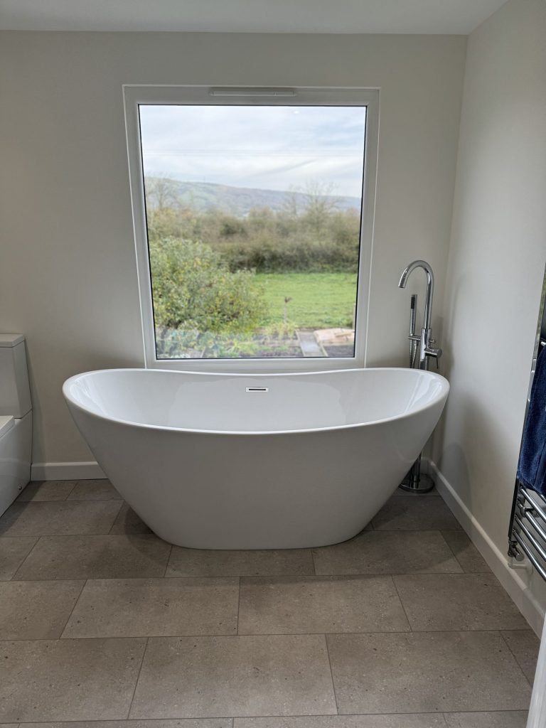 Loft bathroom with a freestanding bath beneath a window onto open fields