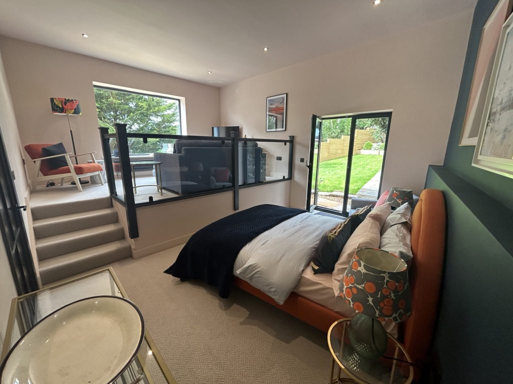 Loft bedroom with a green feature wall, mezzanine steps and a glazed gable onto the garden