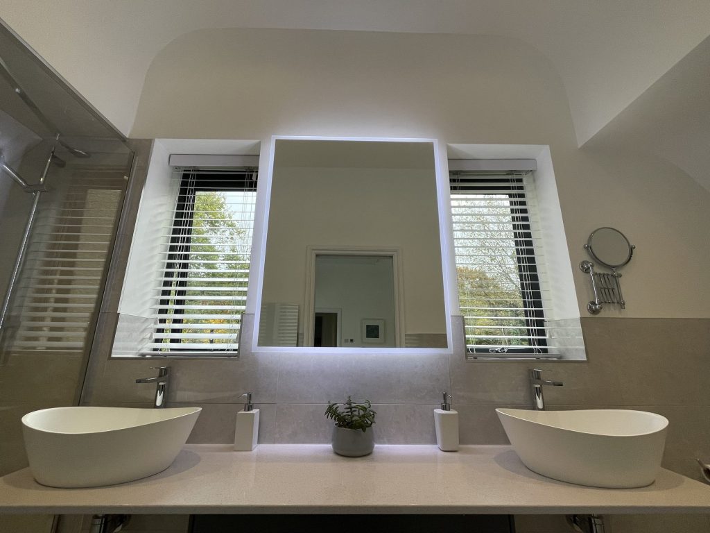 Loft en-suite with twin stone basins, a backlit mirror and shuttered windows