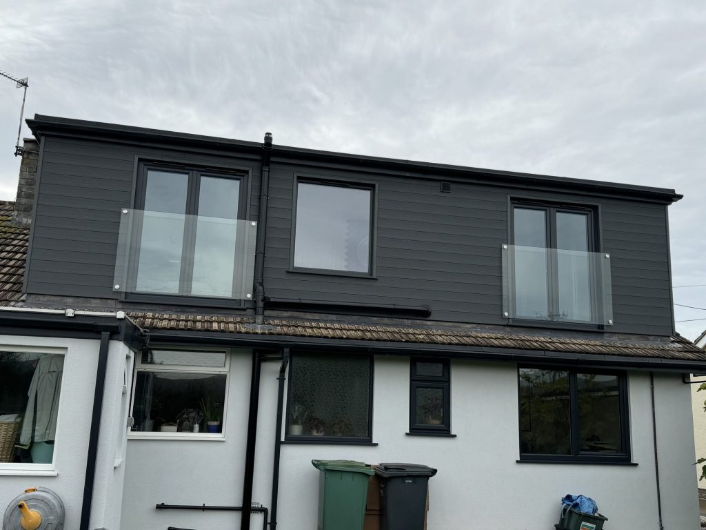 Rear elevation of a house after a dormer loft conversion, with dark grey cladding, full-height windows and glass Juliet balconies above the original white render.