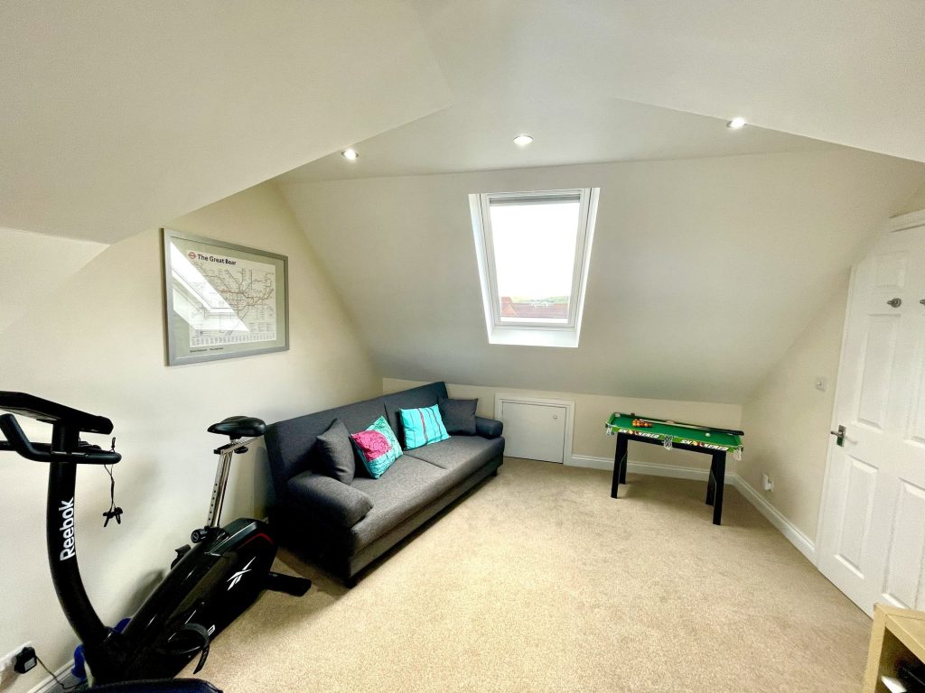 Loft room used as a family sitting and games space, with a Velux roof window, a sofa, an exercise bike and a small table-football table under the sloped ceiling.