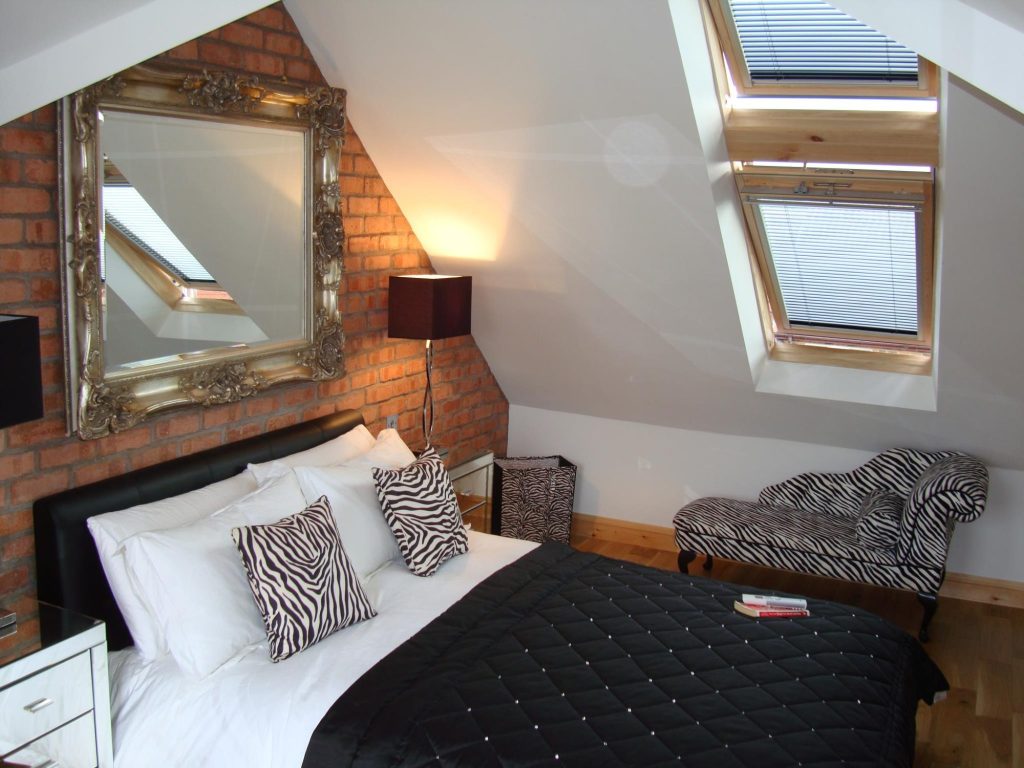 Loft bedroom with an exposed brick chimney breast, gilt mirror and Velux windows