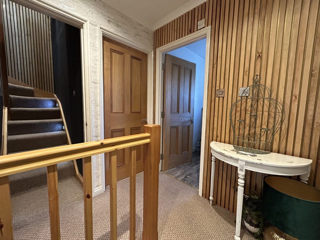 Loft landing at the top of a new staircase, with an oak balustrade, oak slatted wall panelling and a panelled door through to the loft room.
