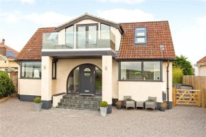 Rendered detached house after a loft conversion, with a gabled front, a glass balcony and a rooflight set into the tiled roof