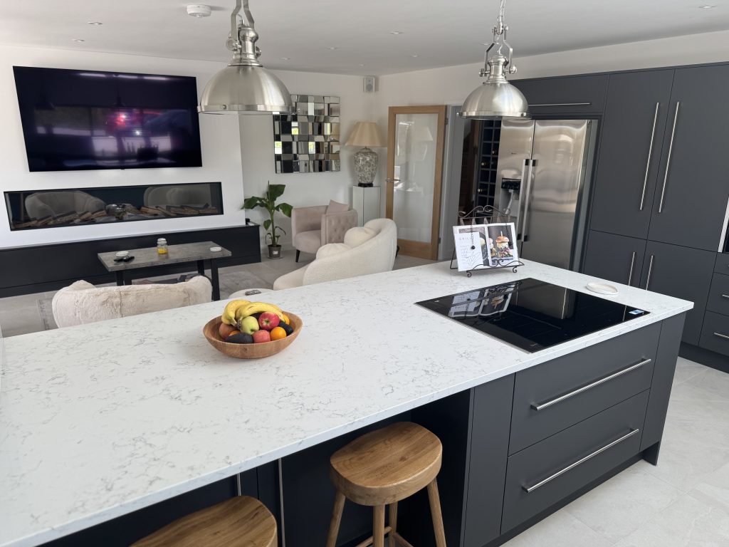 Renovated open-plan kitchen and living space with a navy island, marbled quartz worktop and an inset fire beyond