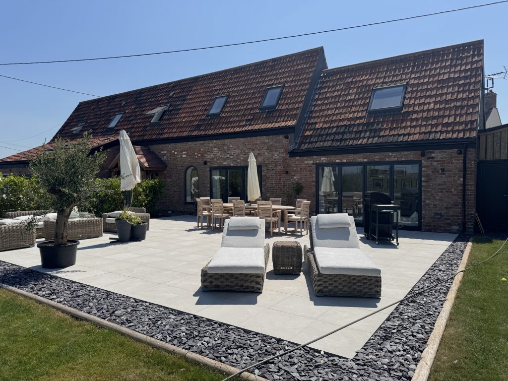 Converted brick barn with black-framed glazing, rooflights and a porcelain-paved terrace with outdoor seating
