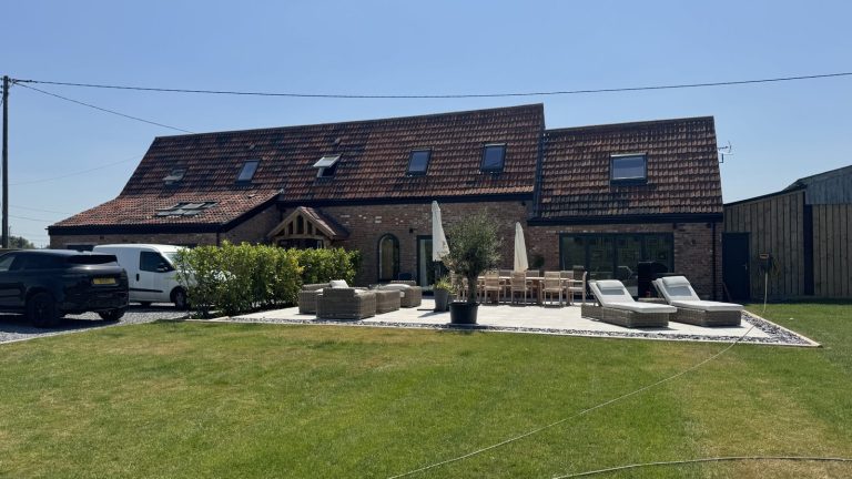 The same house after renovation, with a new tiled roof and dormer, glazed doors and a porcelain terrace laid out for dining and lounging