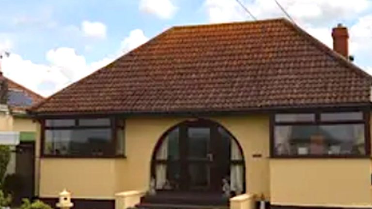 Cream rendered bungalow with a low tiled roof and an arched porch, before its loft conversion