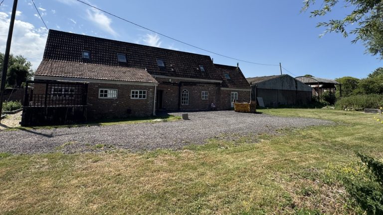 Brick house with a dark weathered roof, loose gravel and a patchy lawn before renovation
